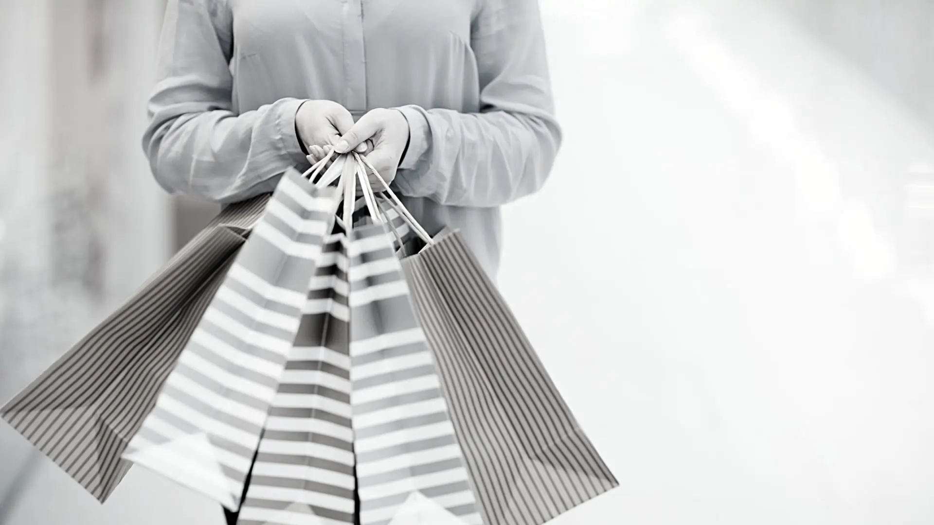 Mulher à esquerda segurando quatro sacolas de compra, representando o consumo que é tributado por meio dos impostos sobre consumo e serviço.