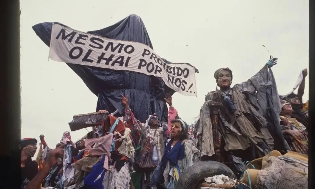 Faixa de desfile escrito "mesmo proibido, olhai por nós"