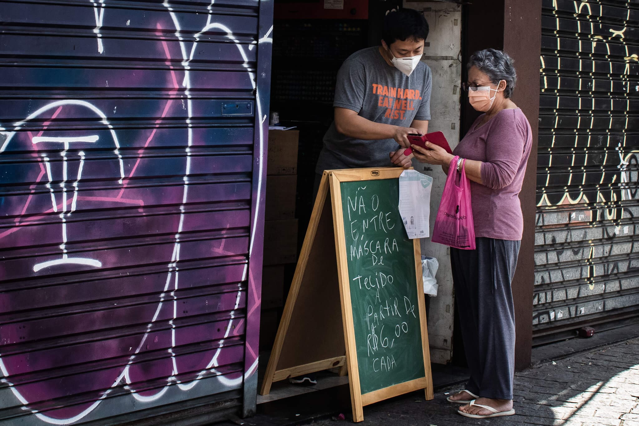 Na imagem, homem e mulher com máscaras conversando na entrada de um estabelecimento. Conteúdo sobre pandemias