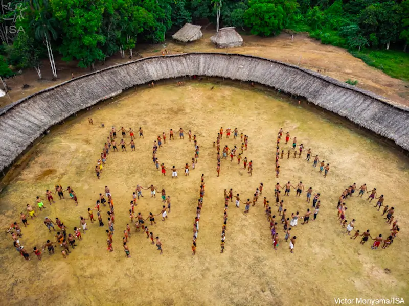 A imagem é uma foto área que mostra vários indígenas agrupados de modo a formar a seguinte frase: "FORA GARIMPO"