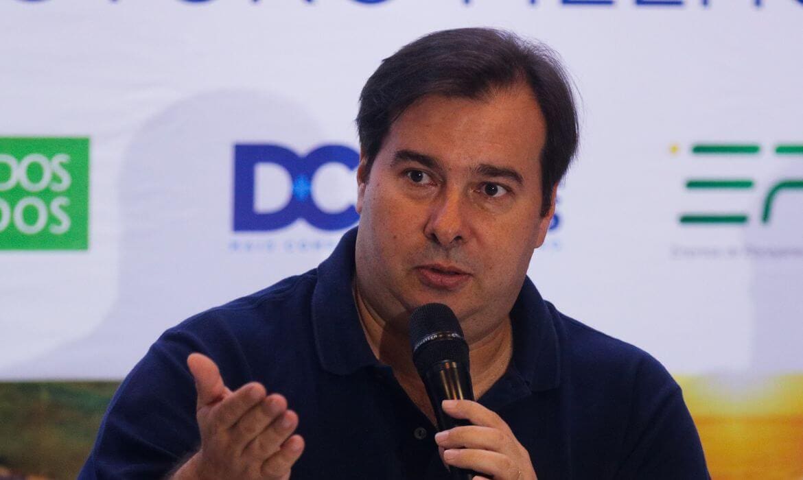 Na imagem, Rodrigo Maia segurando microfone. Conteúdo sobre "economia de guerra"