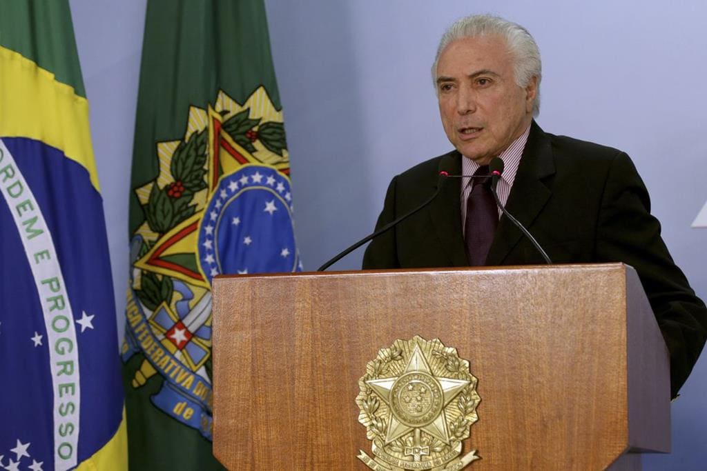 Michel Temer discursa em púlpito de madeira. Ao fundo, as bandeiras do Brasil.