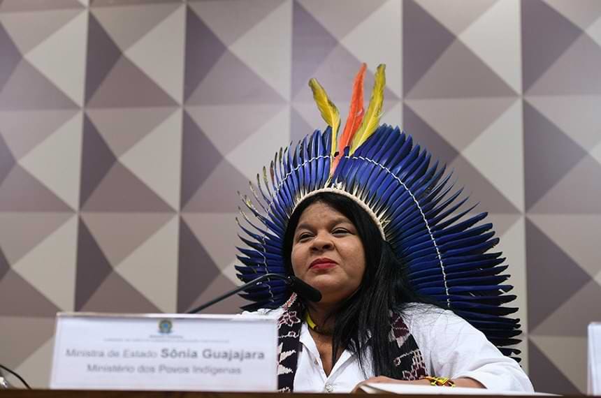 Foto de Sonia Guajajara na Câmara dos deputados discurcusando utilizando um cocár de penas azuis.