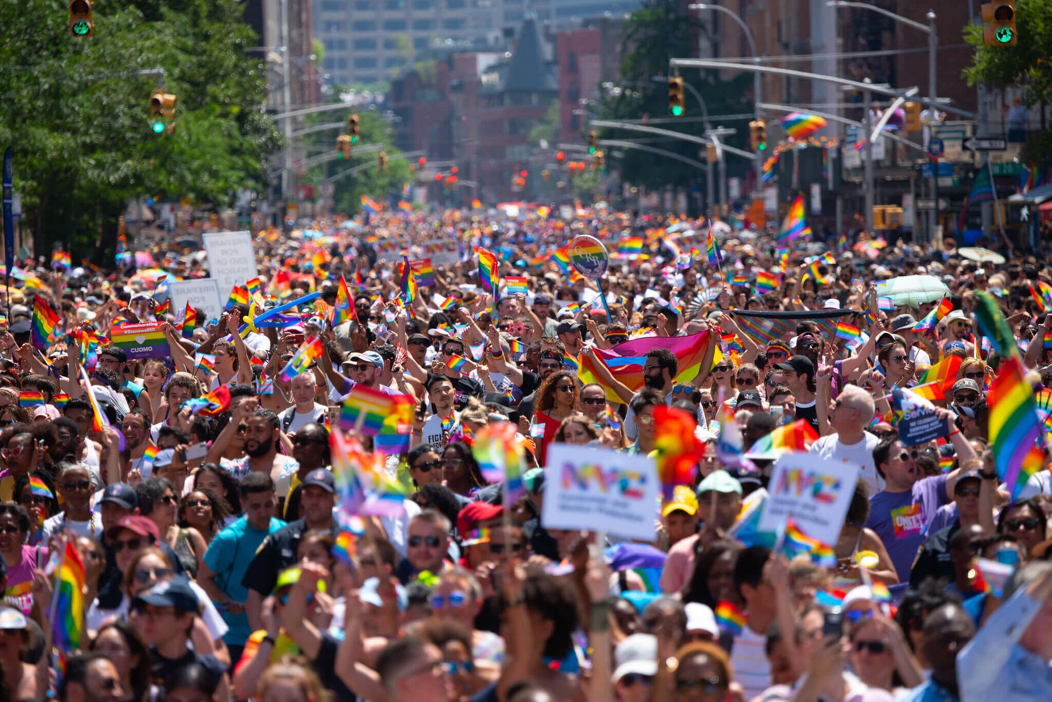 Na imagem, foto de várias pessoas durante marcha Lgbt com bandeiras. Conteúdo representatividade